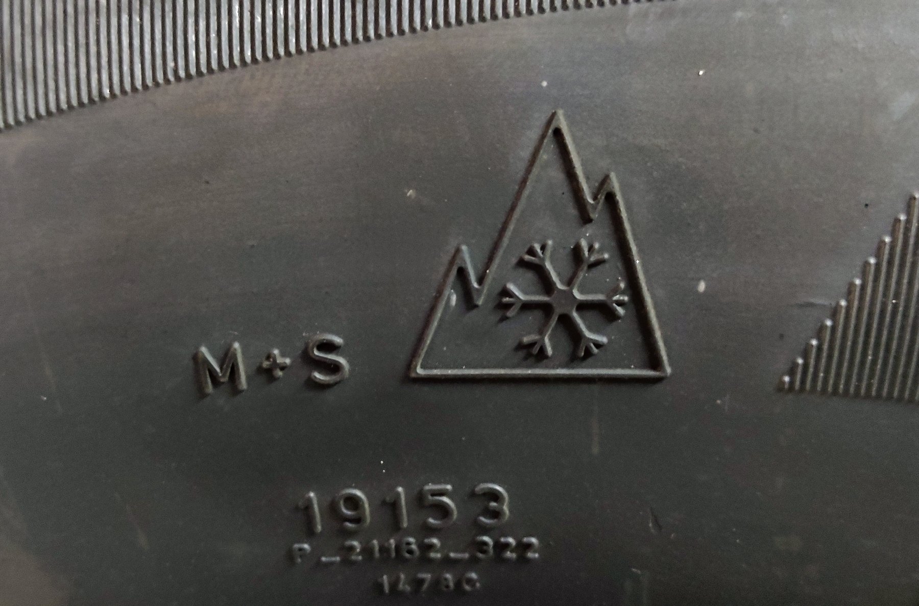 Echtes Alpine-Symbol mit drei Bergspitzen und Schneeflocke auf der Seitenwand eines Winterreifens, daneben M+S